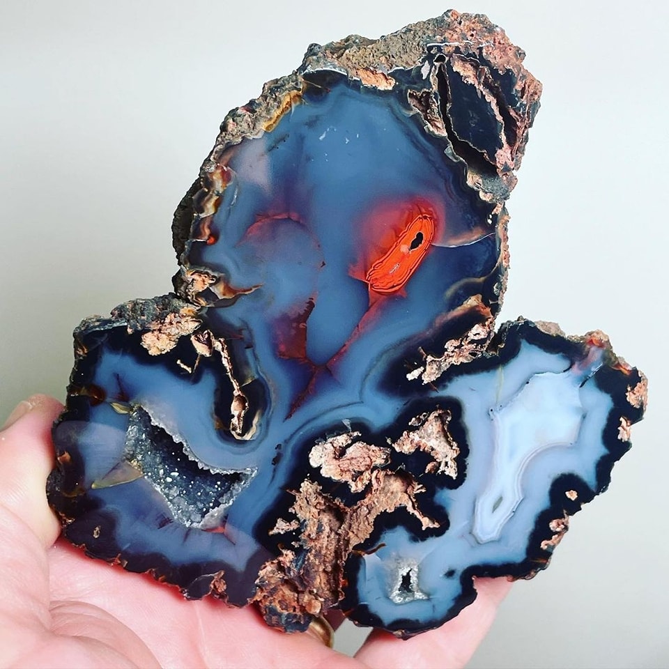 Translucent blue agate mineral slice with red inclusions held in hand