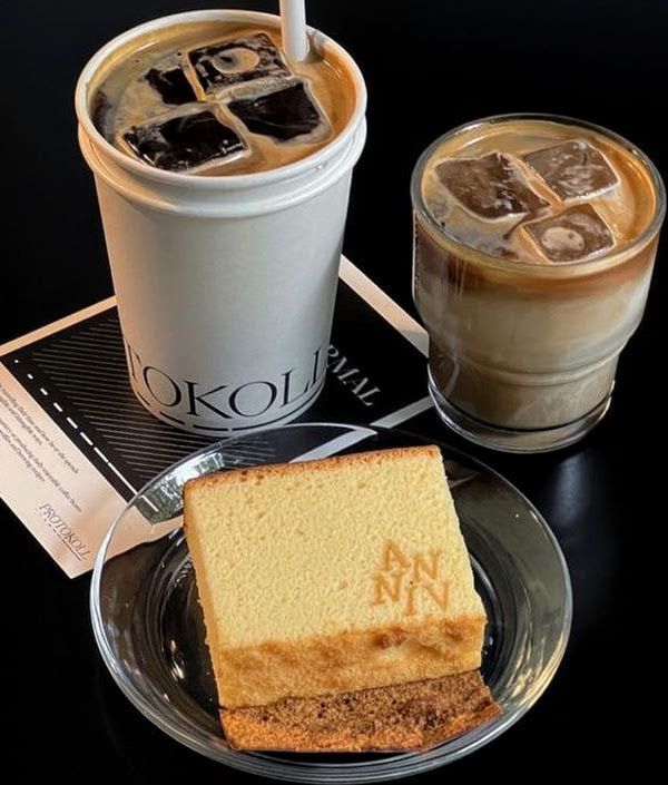 Two iced coffee drinks and a slice of sponge cake on a glass plate against a dark background