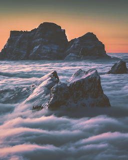 Dark rocky peaks emerging from a thick layer of clouds during sunset with warm sky colors