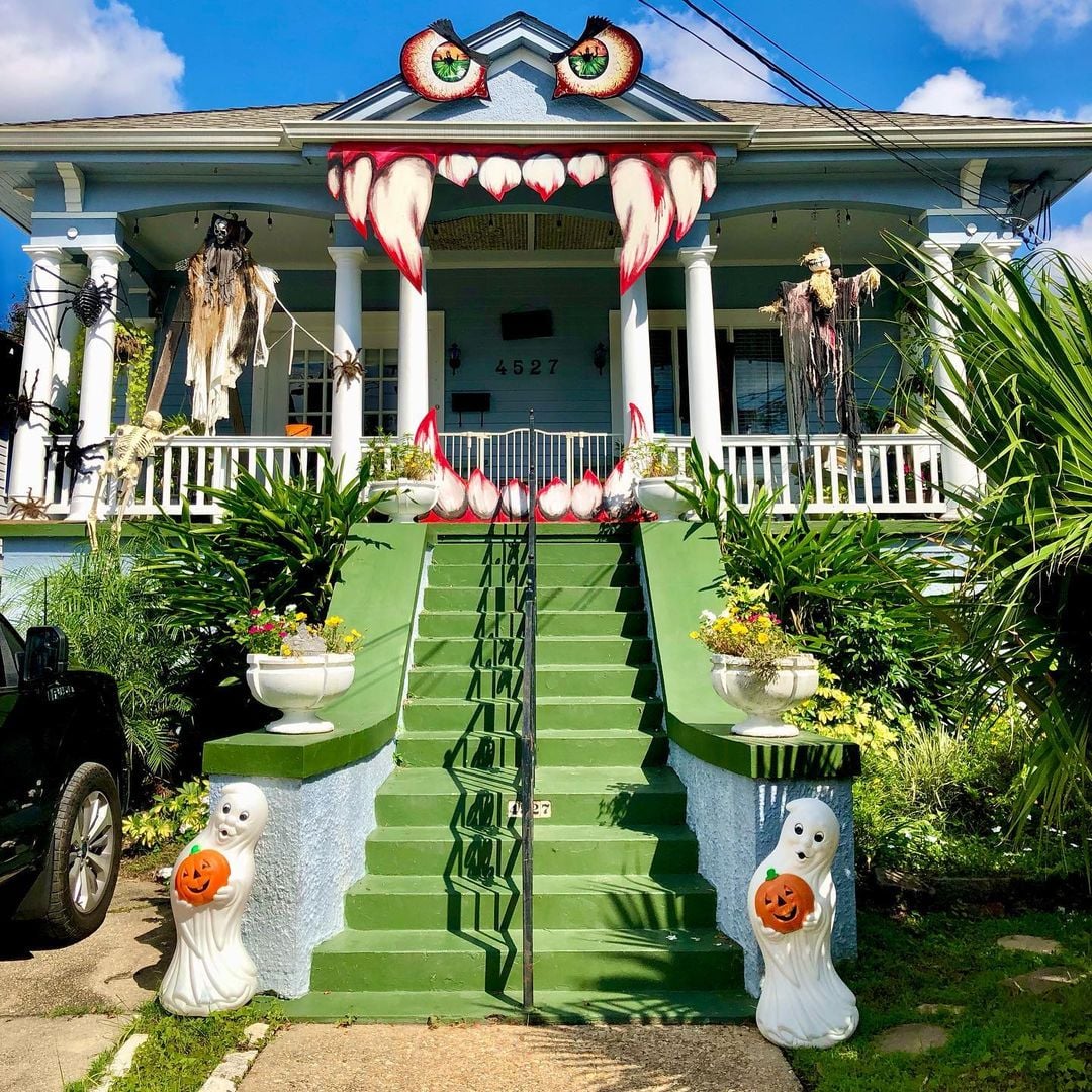 House decorated as green monster with fangs, eyes on roof, Halloween ghosts and pumpkins on lawn