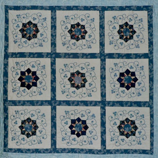 Handmade quilt with blue star blocks in a 3x3 grid pattern with decorative floral elements and teal borders