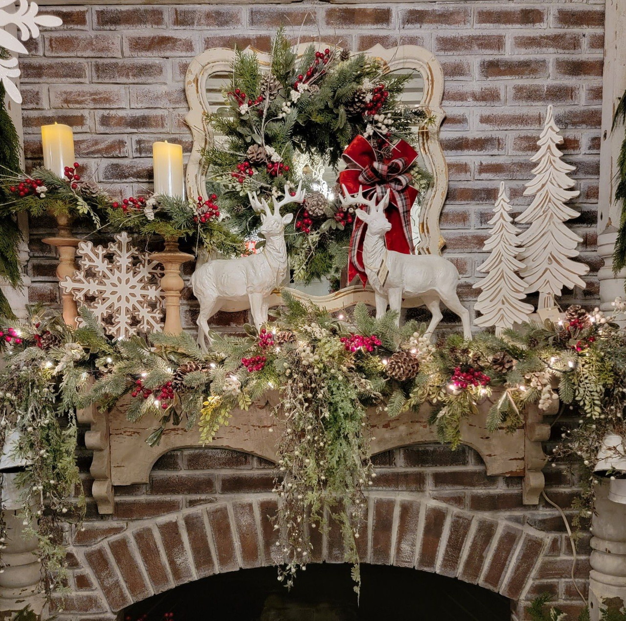 Christmas mantle with white reindeer, garland, candles, and decorative trees on brick fireplace