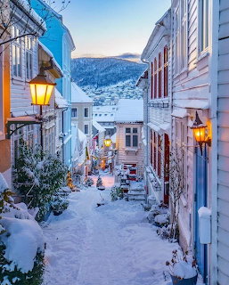 Snow-covered narrow street in Bergen with colorful wooden buildings and lit lanterns