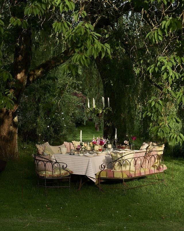 Elegant outdoor dining table with cushions and candles set under green trees in a garden