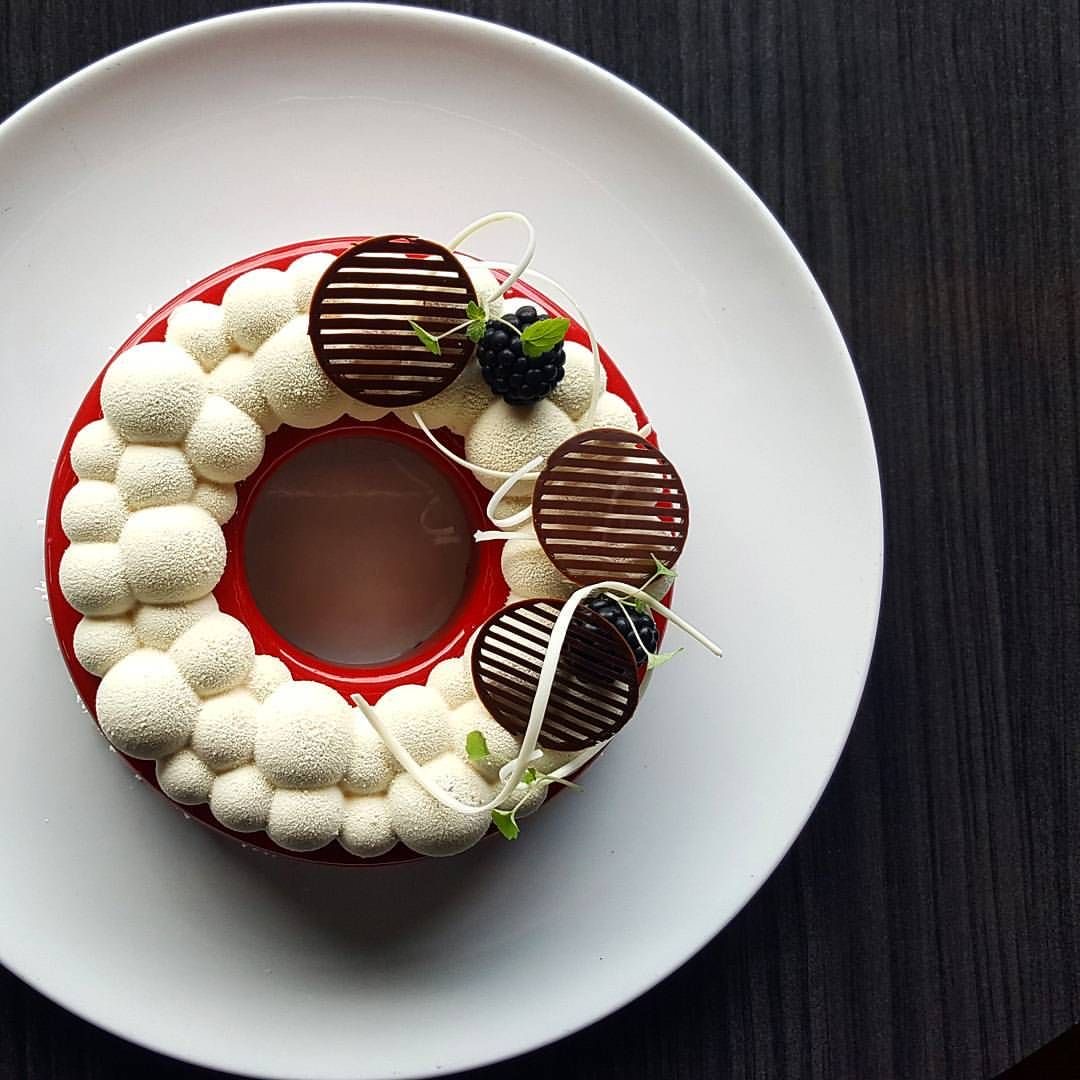 Ring-shaped chocolate dessert with white cream piping and chocolate decorations on white plate