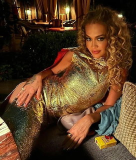 Woman with curly blonde hair in a gold sequined dress posing outdoors at night