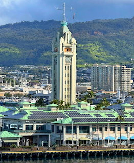 Aloha Tower clock tower in Honolulu with green-rofed buildings and lush mountains behind