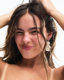 Young woman with brown hair smiling playfully with hands in her hair wearing bear earings