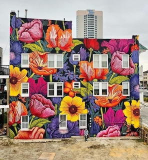Apartment building covered in colorful floral mural with pink, orange, and yellow flowers painted around windows