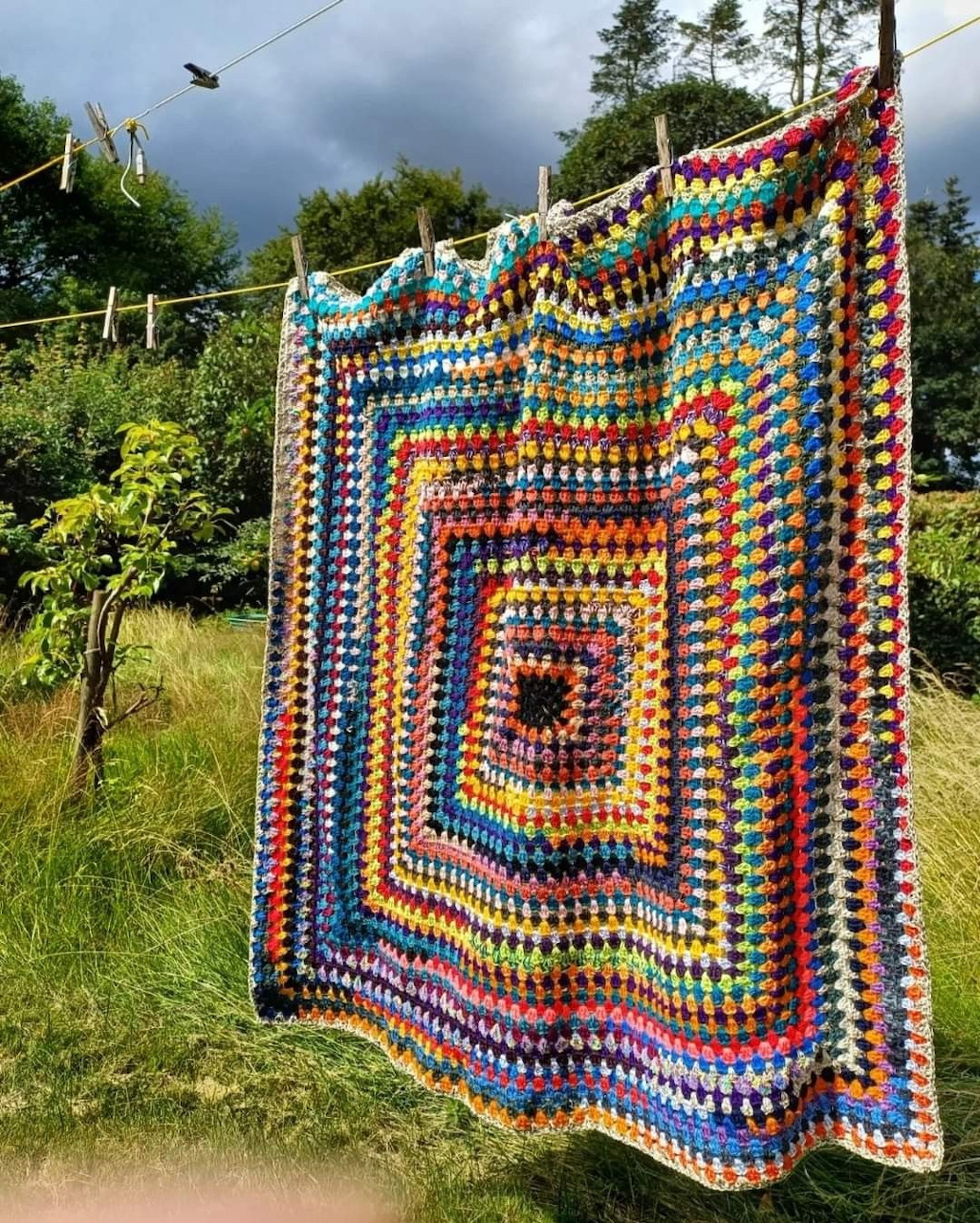 Colorful crocheted granny square blanket hanging on a clothesline in a green garden