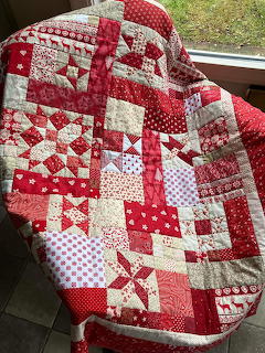 Red and white patchwork quilt with floral and polka dot patterns draped over dark surface near window