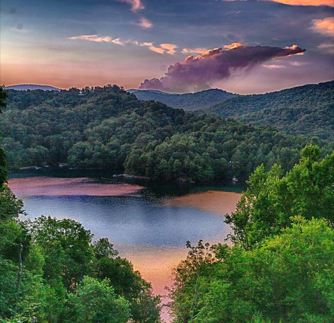 Scenic lake view at sunset with forested mountains and colorful sky reflection