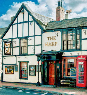 White Tudor-style pub named The Harp with black timber framing and red British phone box beside entrance