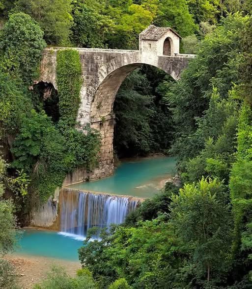 Stone arch bridge Ponte di Cecco over turquoise river with waterfall surrounded by green trees in Ascoli Piceno Italy