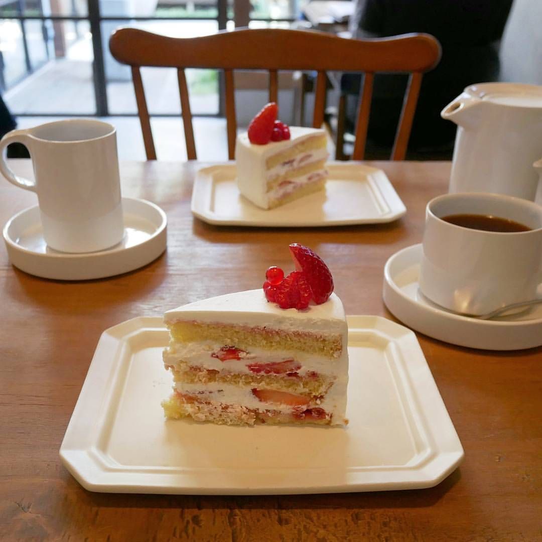 Two slices of strawberry layer cake with coffee cups on a wooden table