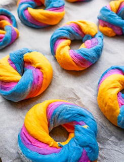 Rainbow-colored bagels with swirled multi-color dough arranged on white surface