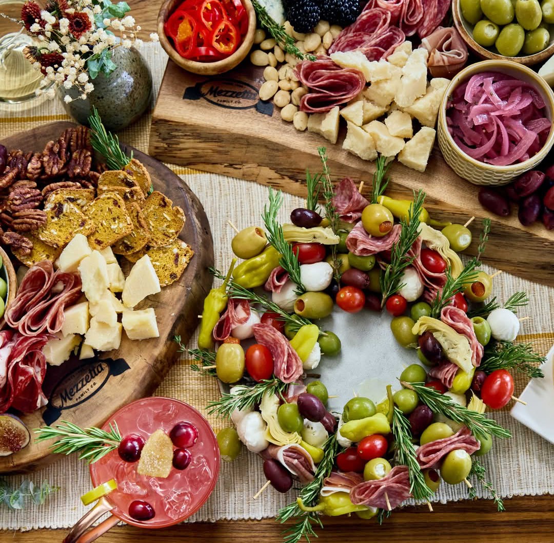 Holiday charcuterie wreath with cheese, olives, cured meats, tomatoes, and herbs on a wooden table