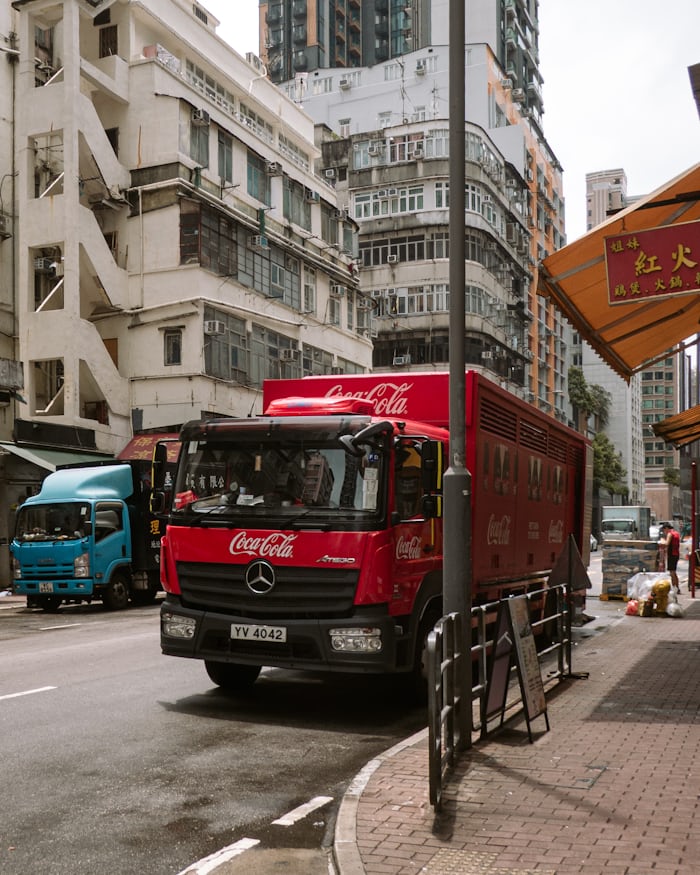 Red Coca-Cola delivery truck on a busy Hong Kong city street with tall buildings in the background