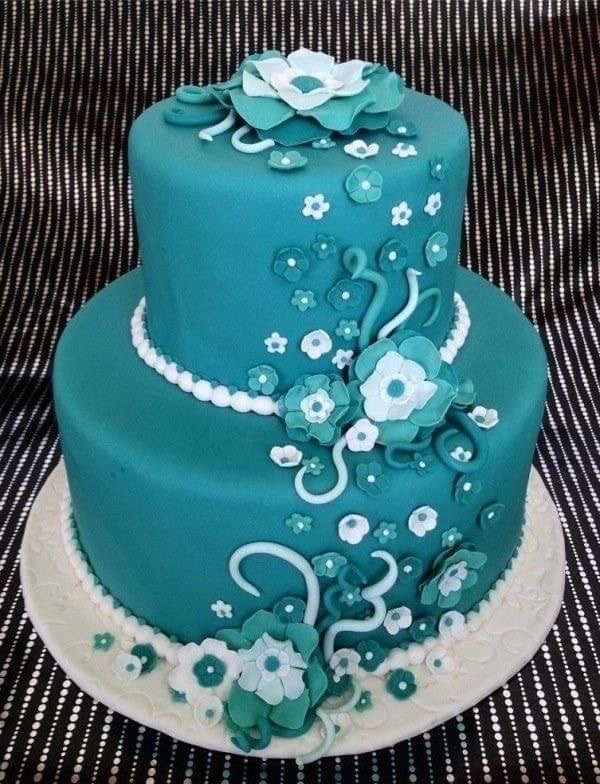 Teal two-tier cake with white and blue floral decorations on a black textured background