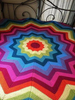 Colorful crocheted star blanket with rainbow concentric rings displayed on an iron bed frame
