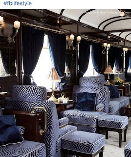 Luxurious train carriage with blue patterned seats, dark wood trim, and curtained windows