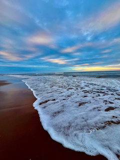Foamy ocean wave on a sandy beach under a blue cloudy sky