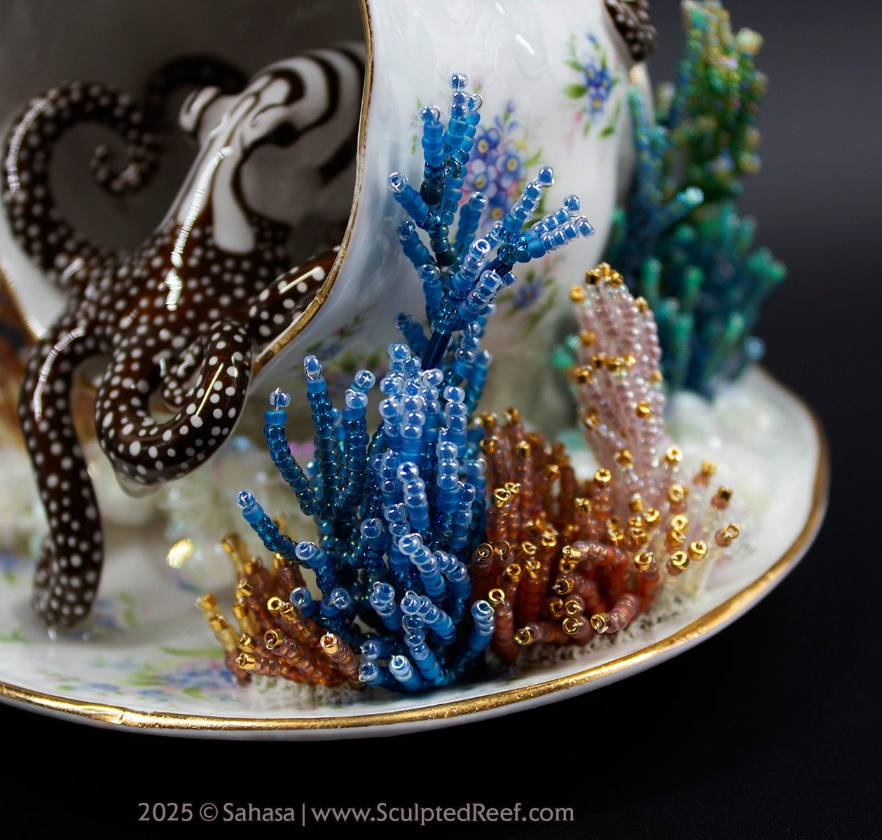 Beaded octopus sculpture emerging from a tipped teacup with blue and gold coral-like bead decorations