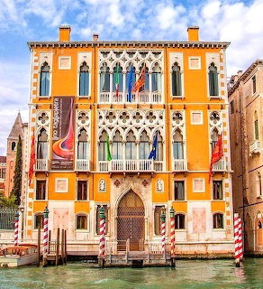 Ornate orange Venetian palazzo with Gothic arches and decorative facade on canal with mooring posts