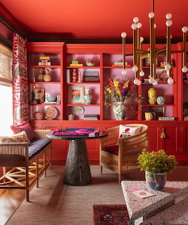 Red sitting room with built-in shelves, wicker chairs, round table, and flower arrangements