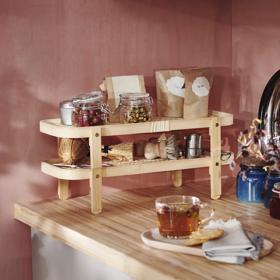 Wooden shelves with glass storage jars and white containers above tea cup on counter in pink-walled kitchen