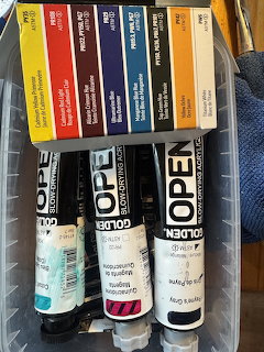 Several tubes of Golden Open acrylic paint in various colors stored in a plastic bin