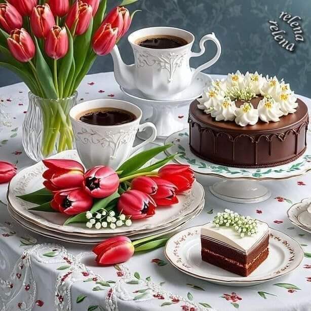 Chocolate cake with white frosting flowers, coffee cups, and red tulips on floral tablecloth