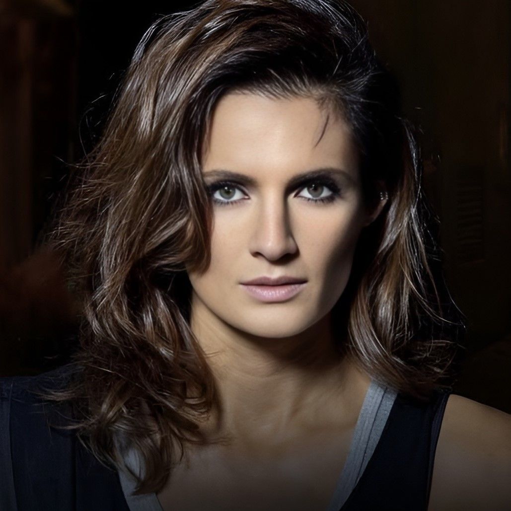 Close-up portrait of a brunette woman with wavy hair and smoky eye makeup against a dark background