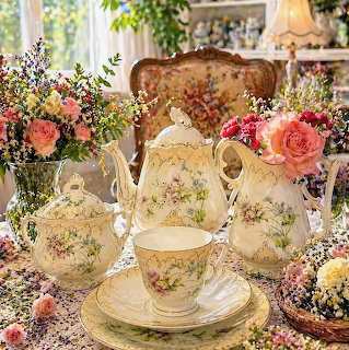 Vintage floral china tea set with teapot, cups, and saucers surrounded by pink roses and white flowers