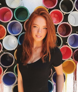 Red-haired woman posing in front of colorful open paint cans