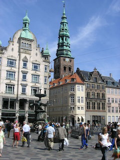 Copenhagen city square with historic buildings, green church spire, and pedestrians on a sunny day