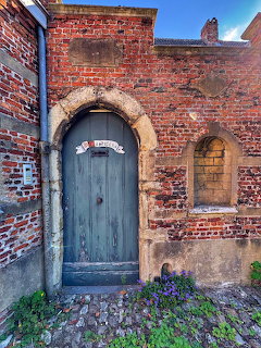 Weathered blue door in brick archway with cobblestones and purple flowers
