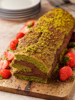 Chocolate pistachio Swiss roll cake on a wooden board with strawberries
