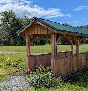 Wooden pavilion with green roof in a grassy park with mountains and trees in the background