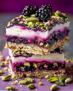 Stacked layered dessert bars with blackberries, pistachios, and white cream filling on purple background
