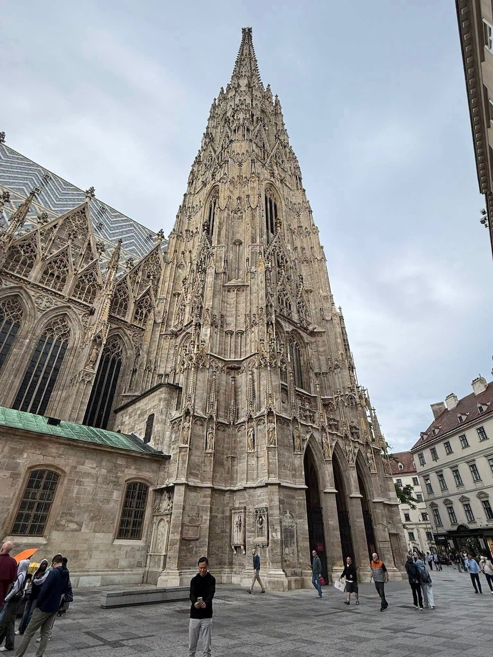 Ornate Gothic cathedral spire in a city square under a cloudy sky