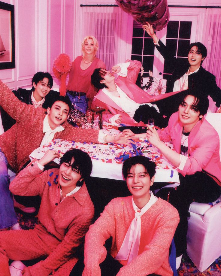 Group of young men in pink outfits celebrating around a confetti-covered table with balloons