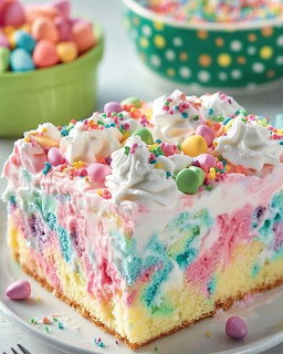 Square slice of rainbow poke cake with pink frosting, whipped cream, and colorful sprinkles