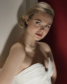 Woman in white strapless dress with gold necklace and updo hairstyle looking at camera