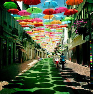 Colorful umbrellas floating above a narrow city street with pedestrians walking below