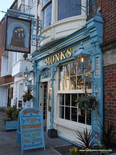 Front entrance of Monks pub with blue facade, hanging sign, windows, and planters.
