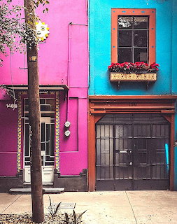 Bright pink and turquoise house facade with dark wooden doors and window box with red flowers