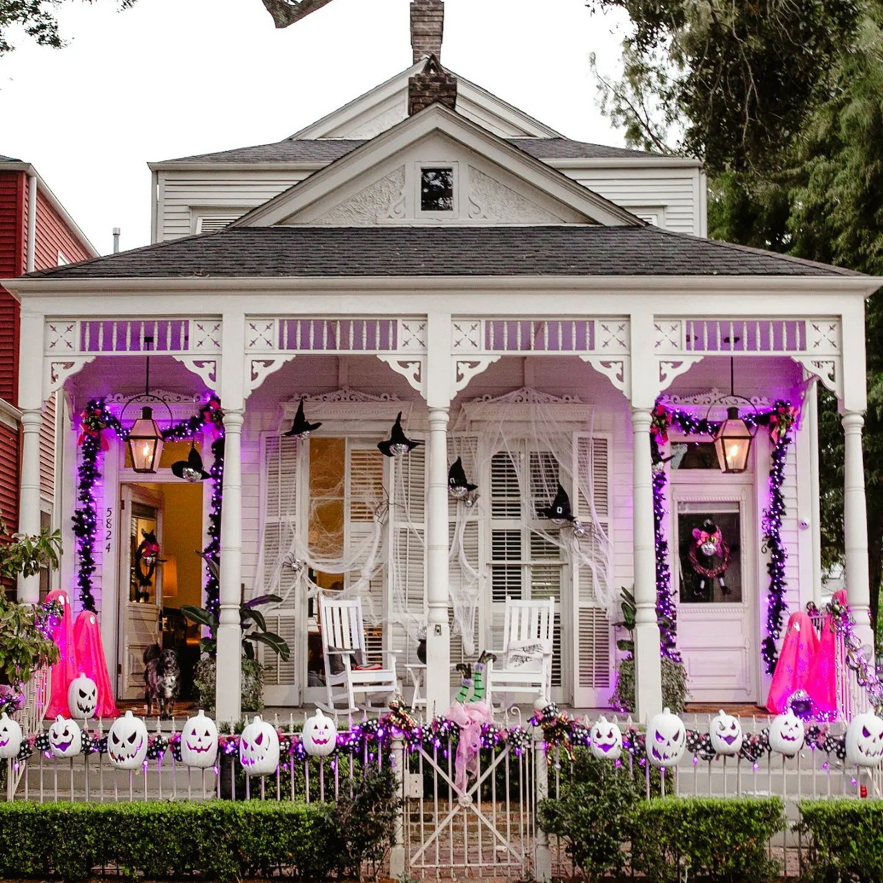 White house with purple and pink Halloween decorations, jack-o'-lanterns, and skeletons on porch