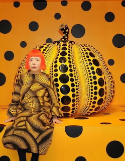 Woman in yellow and black polka dot costume sitting next to giant polka dot pumpkin sculpture on orange polka dot background