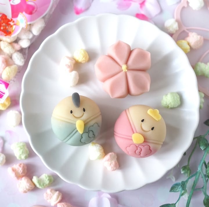 Three cute pastel pastries with smiling faces on a white plate surrounded by candy